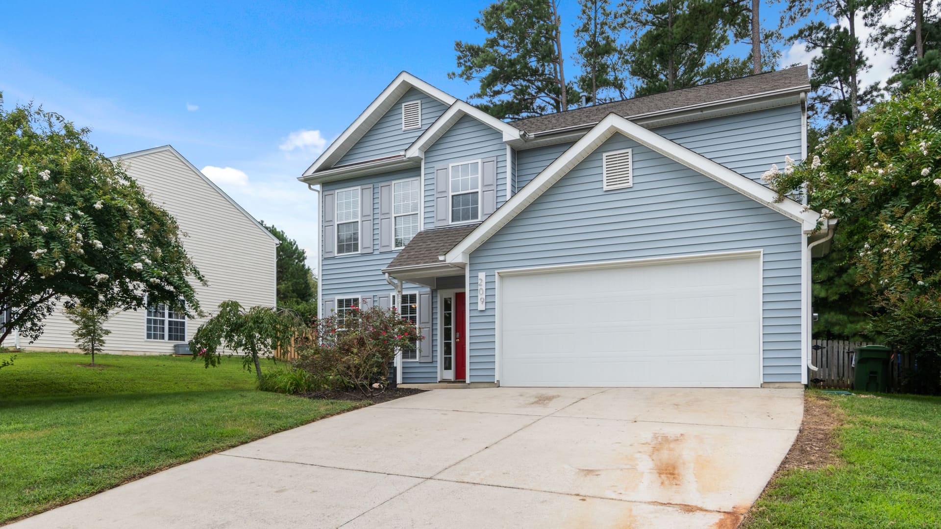 A two-story home with a covered porch and a wide driveway, seen from the street on a clear day.
